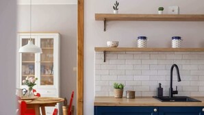 A modern kitchen with white subway tiles, a black faucet, and wooden shelves with kitchen items. - Stylish Apartment | Balcony and Private Parking (Kraków)