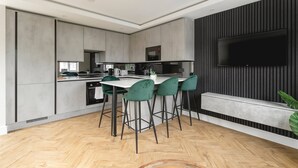 Una cocina moderna con una isla central, taburetes de bar y un televisor de pantalla plana montado en una pared oscura.