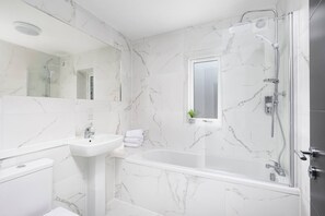 Une salle de bain avec un mur en marbre, un lavabo, une baignoire et une douche.