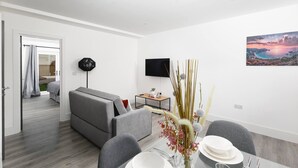 A modern living room with a sofa, dining table, and a flat-screen TV mounted on the wall.