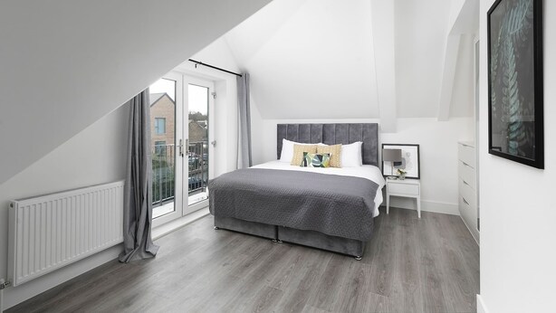 Un dormitorio con techo inclinado, una cama grande, una mesita de noche, un cuadro enmarcado y vistas a través de un puerta de cristal.