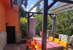 Un espace extérieur aménagé avec une table et des chaises, un coin salon couvert et une vue sur les arbres.