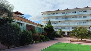 A courtyard with a green lawn, a bench, and a building with multiple balconies.