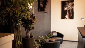 A modern reception area with a dark leather sofa, a potted plant, and a framed artwork on the wall. - Olivia Rooms (Belgrade)