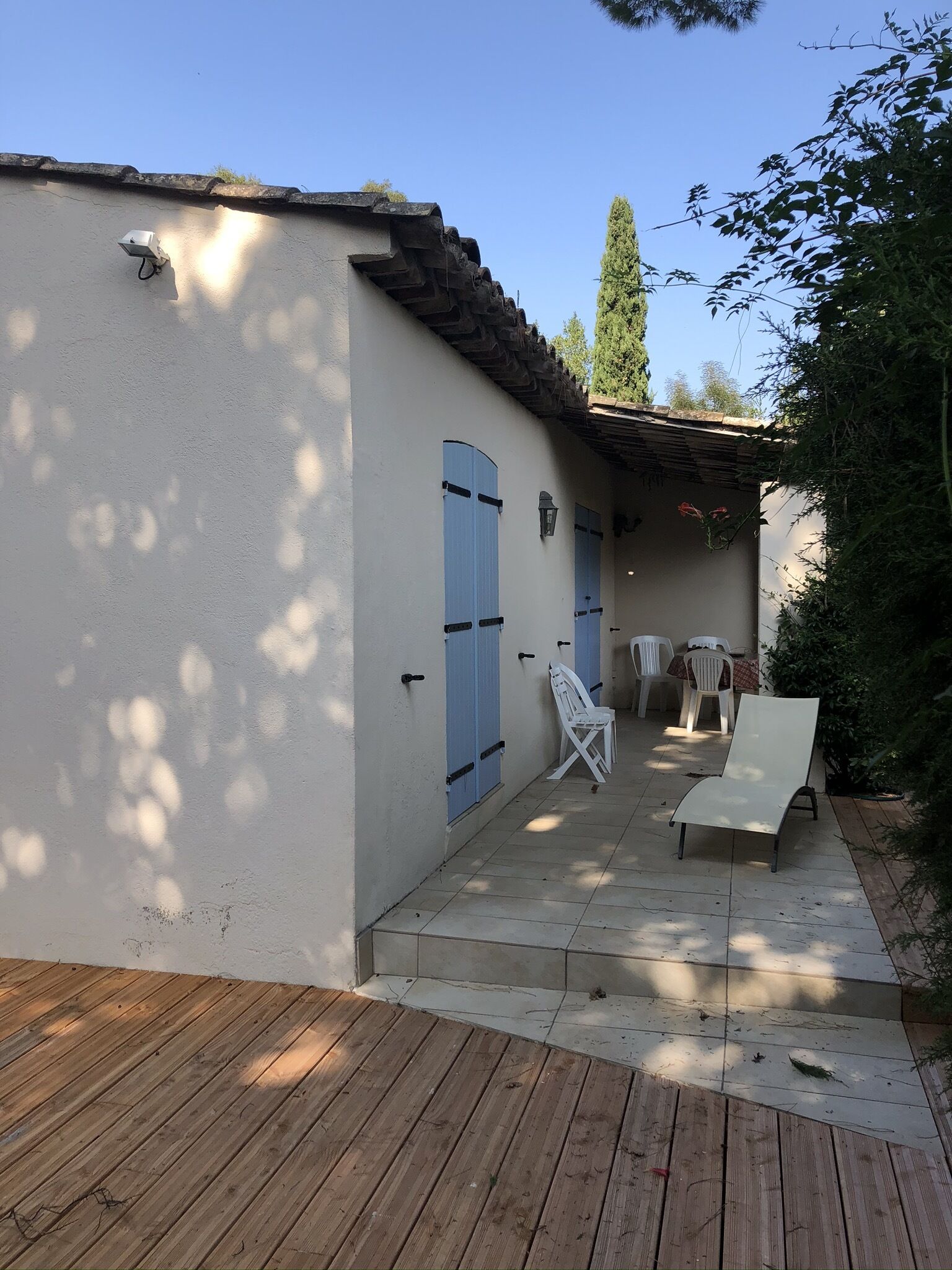 Un bâtiment doté d’un patio carrelé, d’une terrasse en bois et d’un espace détente couvert avec des chaises blanches.
