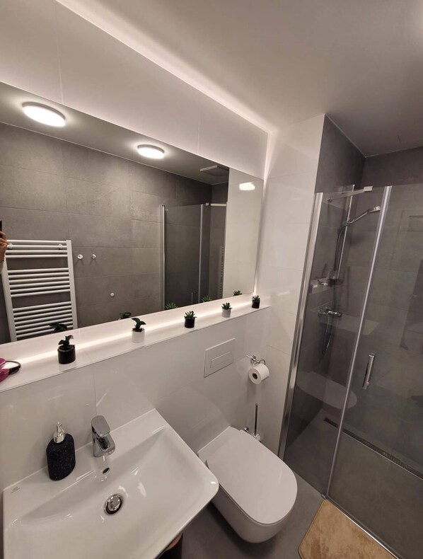 A modern bathroom with a large mirror, a sink, a toilet, and a glass-enclosed shower.