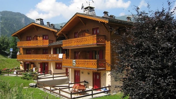 Un chalet traditionnel doté de deux balcons, d’une clôture en bois et surplombant un paysage montagneux.