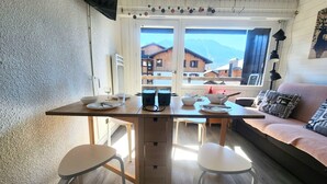 Un comedor con una mesa de madera, dos sillas blancas y un sofá con cojines estampados.