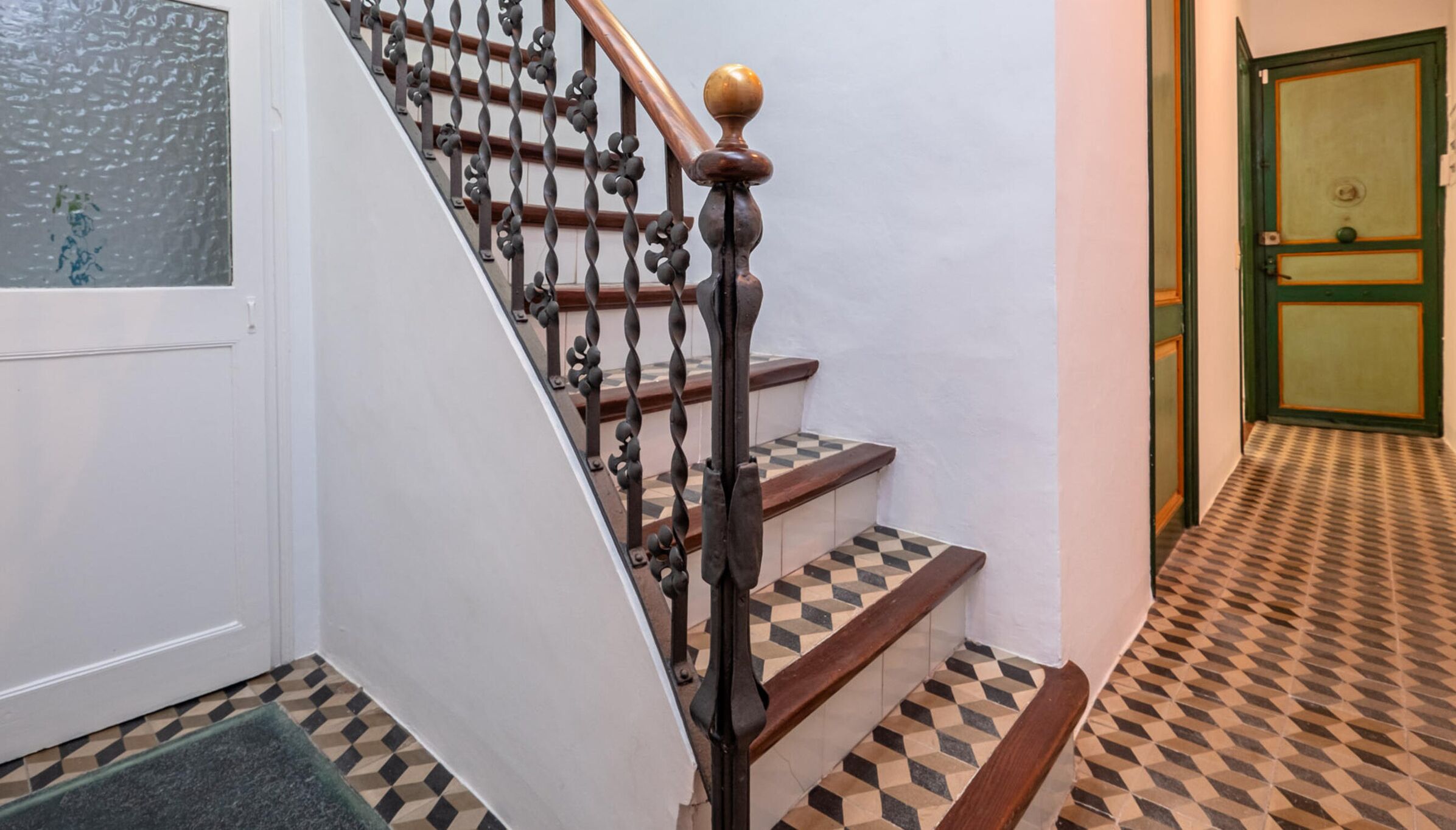 A staircase with a wooden handrail and black balusters, leading to a door with a green frame and a glass panel.