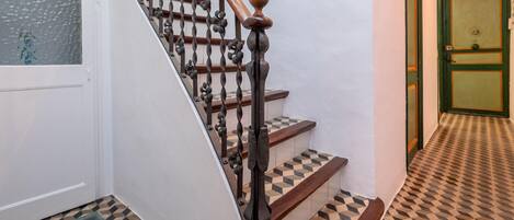 A staircase with a wooden handrail and black balusters, leading to a door with a green frame and a glass panel.
