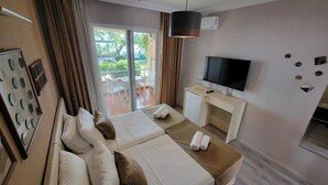 A hotel room with two beds, a TV, a desk, and a view of the outdoors. - Güneş Otel (Edremit)