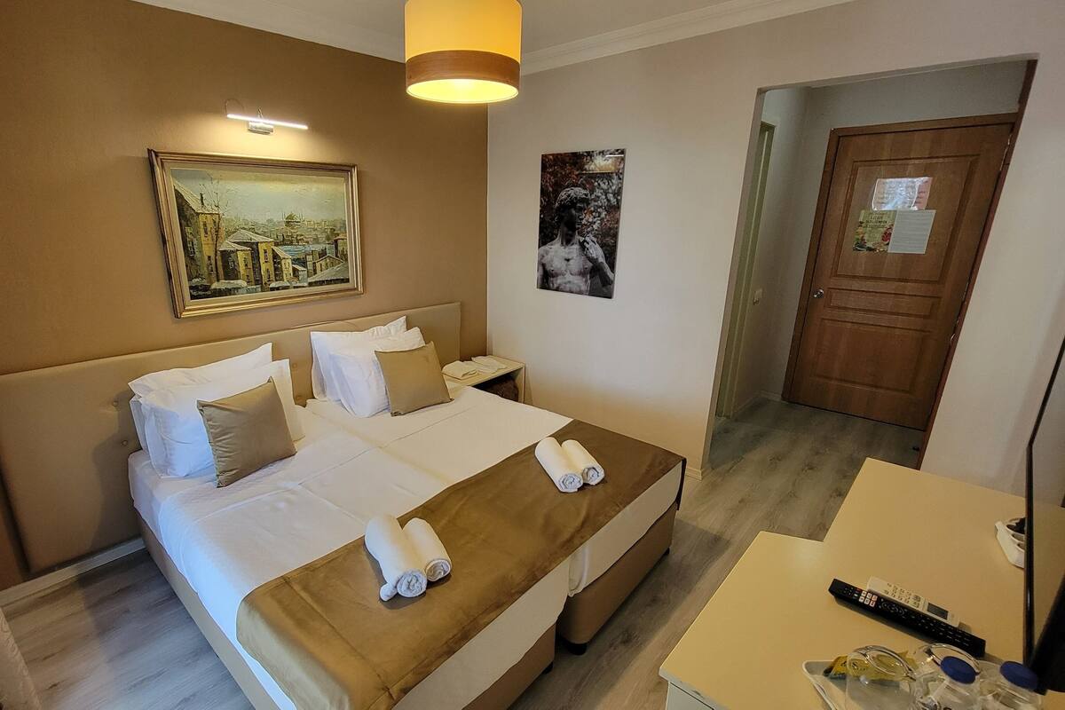 A hotel room with a large bed, a bedside table with a remote control, and a door leading to a hallway.