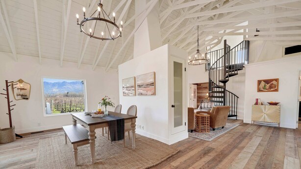 A spacious room with a wooden dining table, a chandelier, and a staircase leading to an upper level. - Villa in French Chateau Estate in Napa Valley (Calistoga)