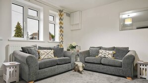 A modern living room with two grey sofas, a small white side table, and a decorative pig sculpture. - Garden Retreat w/ Free Parking & Village Access (Messingham)