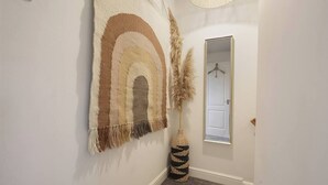 A hallway with a large, striped wall hanging, a tall vase with pampas grass, and a door with a coat rack. - Garden Retreat w/ Free Parking & Village Access (Messingham)