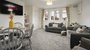 A living room with a grey sofa set, a TV mounted on the wall, and a dining area with a table and chairs. - Garden Retreat w/ Free Parking & Village Access (Messingham)