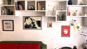 A living room with a green sofa, a bookshelf filled with books and decorative items, and various framed artworks on the wall. - Casa d'Artista - Navigli|Tortona  (Milano)