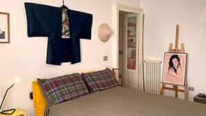 A bedroom with a bed, a hanging robe, a painting on an easel, and a radiator. - Casa d'Artista - Navigli|Tortona  (Milano)