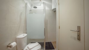 A compact bathroom with a toilet, a glass shower enclosure, and a towel rack. - Alegria Flat City Center by Vacationy (Porto)