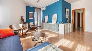 A living room with a blue accent wall, a Buddha statue, a sofa with orange pillows, a wooden coffee table, and a white reception desk with framed artwork. - 3688 Casa Fortuna by Barbarhouse (Gallipoli)