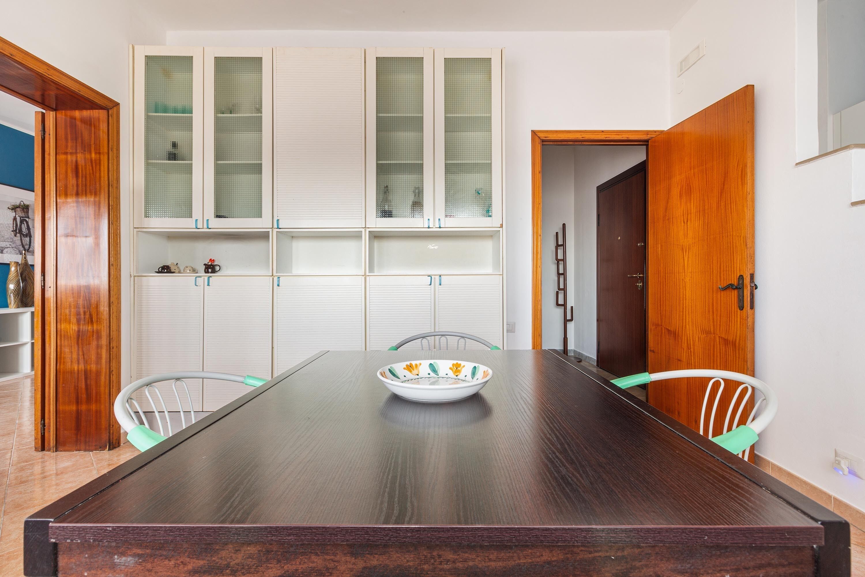A dining area with a long wooden table, white chairs, and a white cabinet with glass doors.