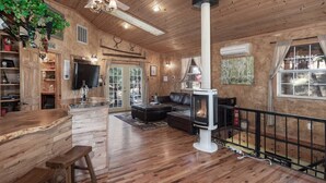 A spacious living area with a fireplace, wooden floors, and a ceiling fan. - Sandoval in the Historic Upper Canyon (Ruidoso)