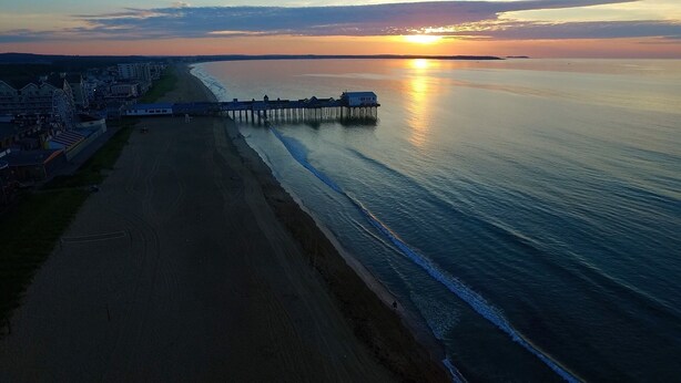 A coastal view with a pier extending into calm waters, a beach, and buildings along the shore. - Gull's Nest by Bayley Vacation Rentals (Old Orchard Beach)