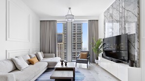 A modern living room with a grey sofa, a coffee table, a TV, and a view of tall buildings through large windows.
