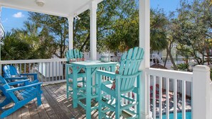 Un espace extérieur abrité, doté de chaises turquoise et d’une table, entouré de rampes blanches et d’arbres.