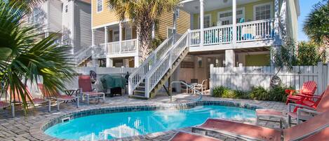 A pool area with lounge chairs and a staircase leading to a balcony.