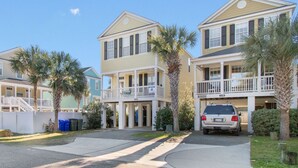 Une rangée de condominiums en bord de mer, avec deux étages, des balcons, un espace de stationnement couvert et des palmiers.
