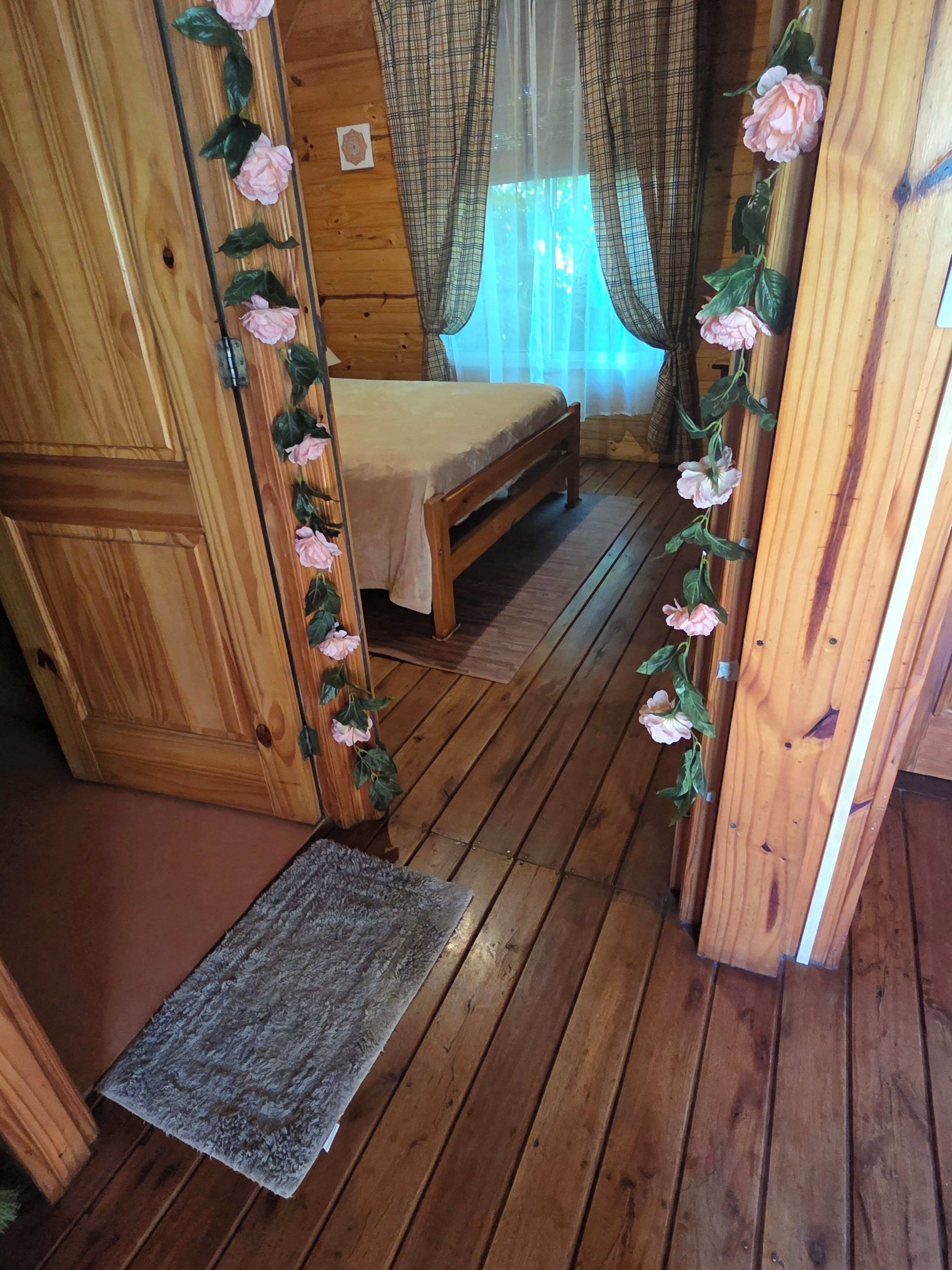 A wooden interior with a bed, curtains, and a floral decoration.