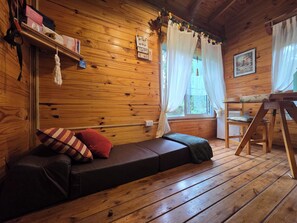 A wooden cabin interior with a sofa, a ladder, and a window with curtains.