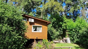 Eine kleine Holzhütte mit Fenster und Klimaanlage, umgeben von üppiger Vegetation und Bäumen.