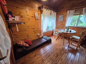 A wooden cabin interior with a sofa, a dining table, and a window with curtains. - Cabaña "Las Casuarinas de Dique Luján" (Dique Luján)