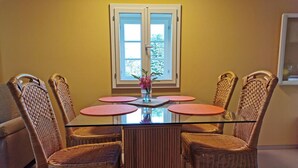 A dining area with a glass-top table, four wicker chairs, and a window with a view of trees. - Im Herzen der Sächsischen Schweiz- Fewo Bloßstock für Max. 5 Personen (Sebnitz)