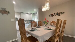 A dining area with a table set for six, wooden chairs, a vase with flowers, and pendant lights. - 2 King Suites Hot Tub Fire Pit Air Hockey 2 (North Charleston)