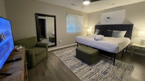 A modern hotel room with a large bed, a green armchair, a flat-screen TV, and a ceiling fan. - 2 King Suites Hot Tub Fire Pit Air Hockey 2 (North Charleston)