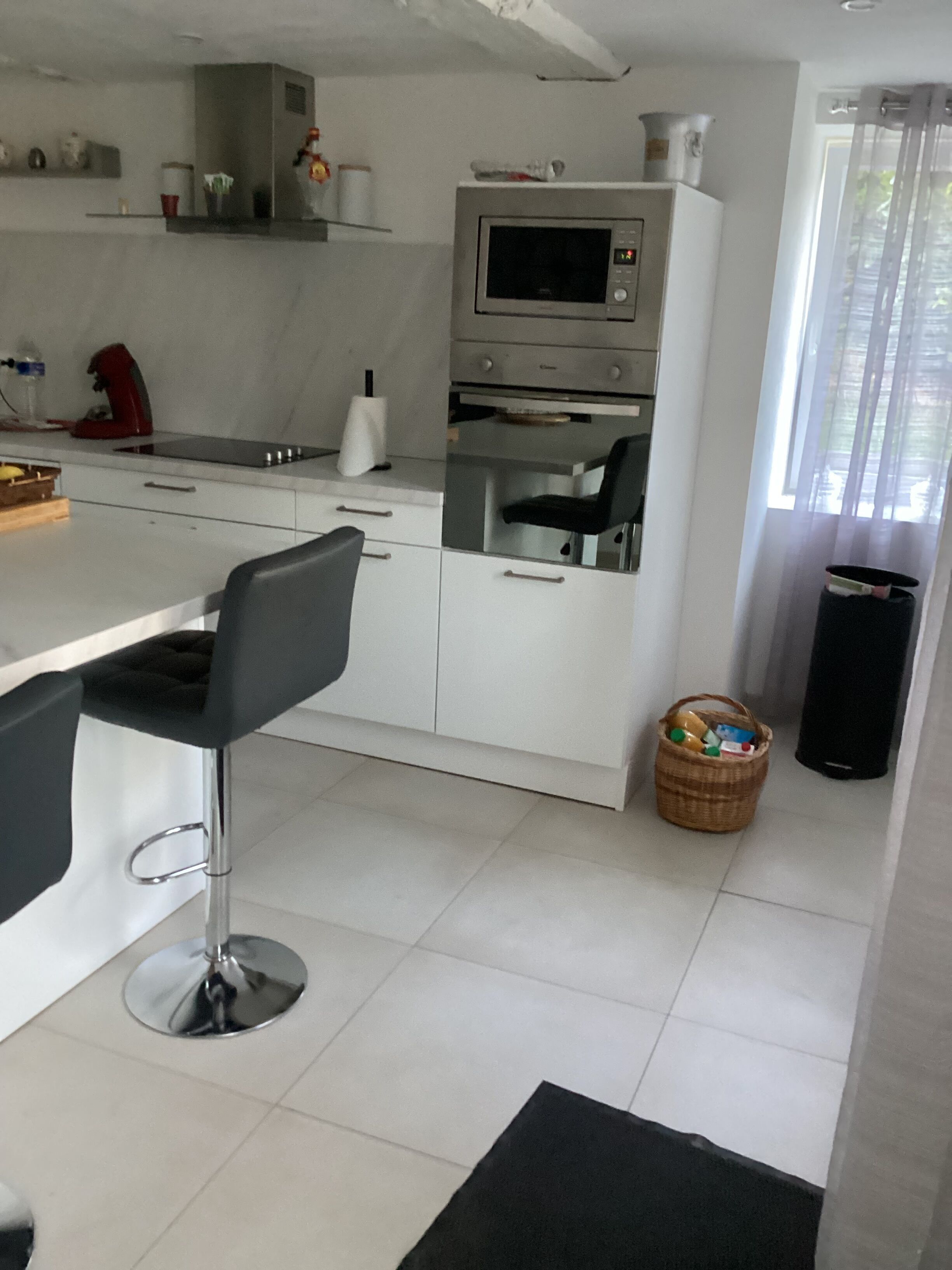 A modern kitchen with white cabinets, a built-in oven, a microwave, and a dining area with a bar stool.