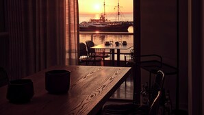 A dining area with a wooden table and chairs, a view of a sunset over water, and a ship in the distance. - Monopolio Waterfront Apartment (Zakynthos)