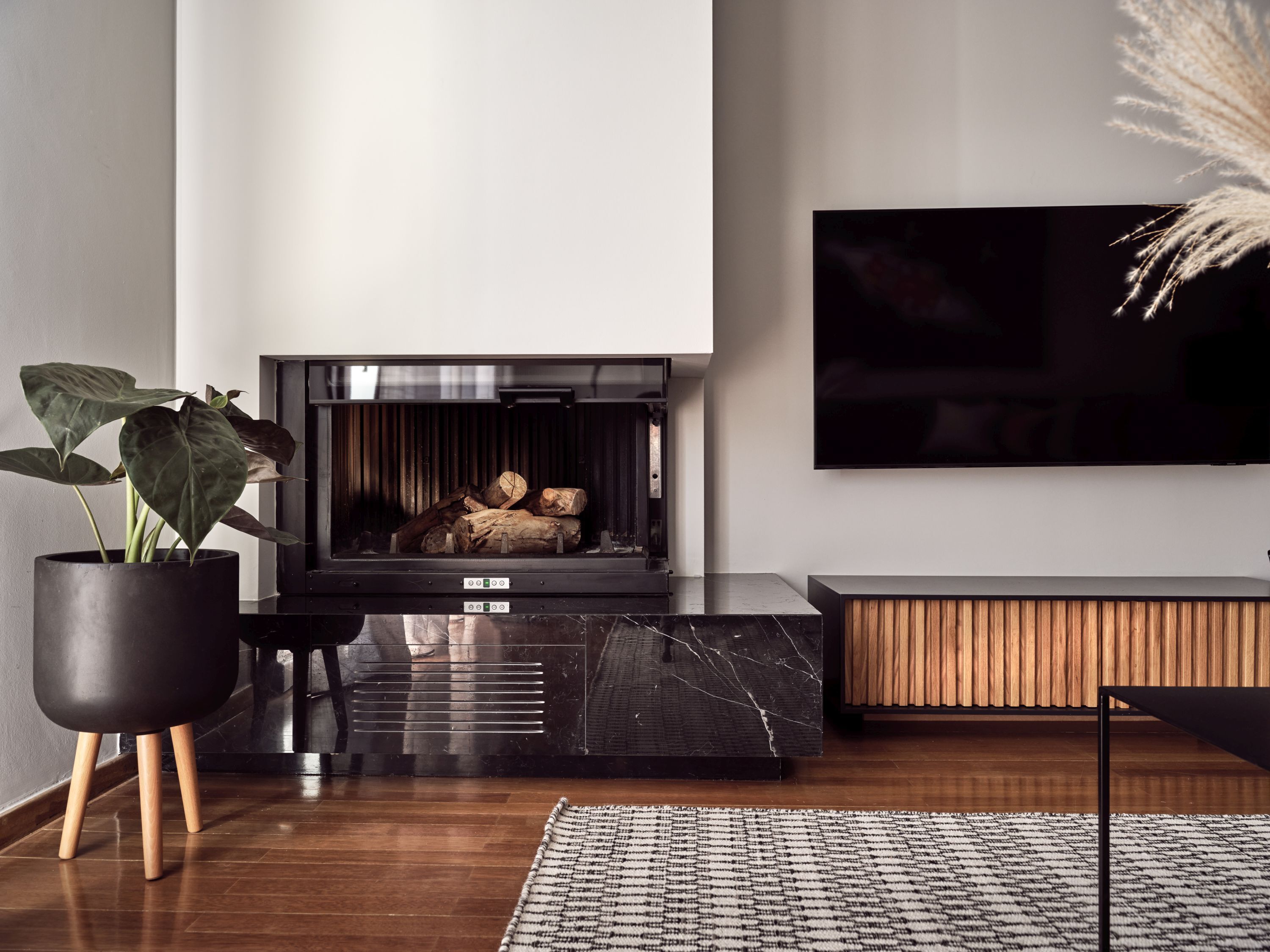 Un salon moderne avec une cheminée, un grand téléviseur à écran plat, une plante en pot et un banc en bois.