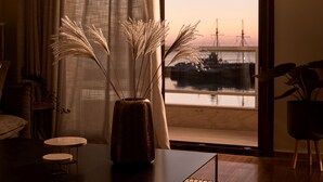 A room with a large window, a vase with dried plants, a small round table, and a chair. - Monopolio Waterfront Apartment (Zakynthos)