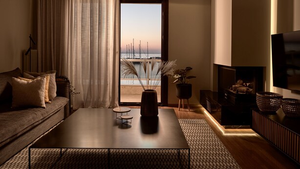 A modern living room with a sofa, coffee table, and TV. A large window offers a view of the sea and boats. - Monopolio Waterfront Apartment (Zakynthos)