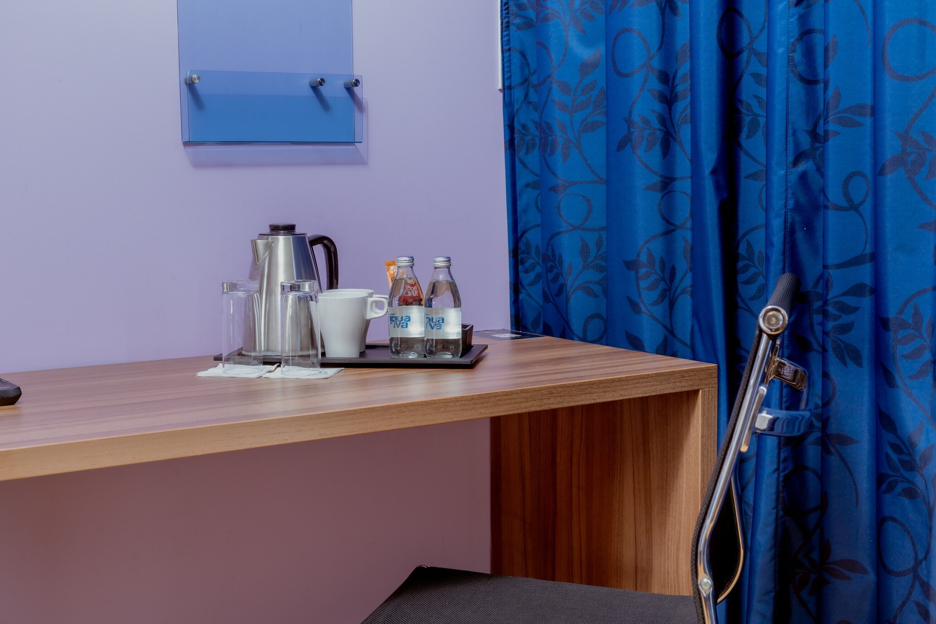 A hotel room with a wooden desk, a coffee maker, cups, and bottles.