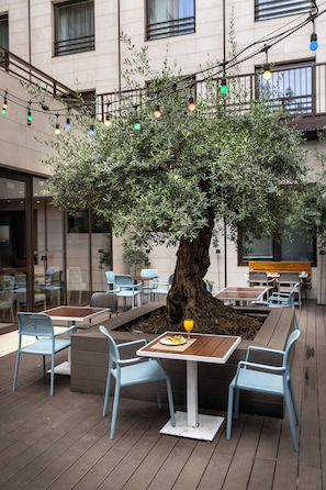 An outdoor seating area with tables and chairs, a tree, and string lights.