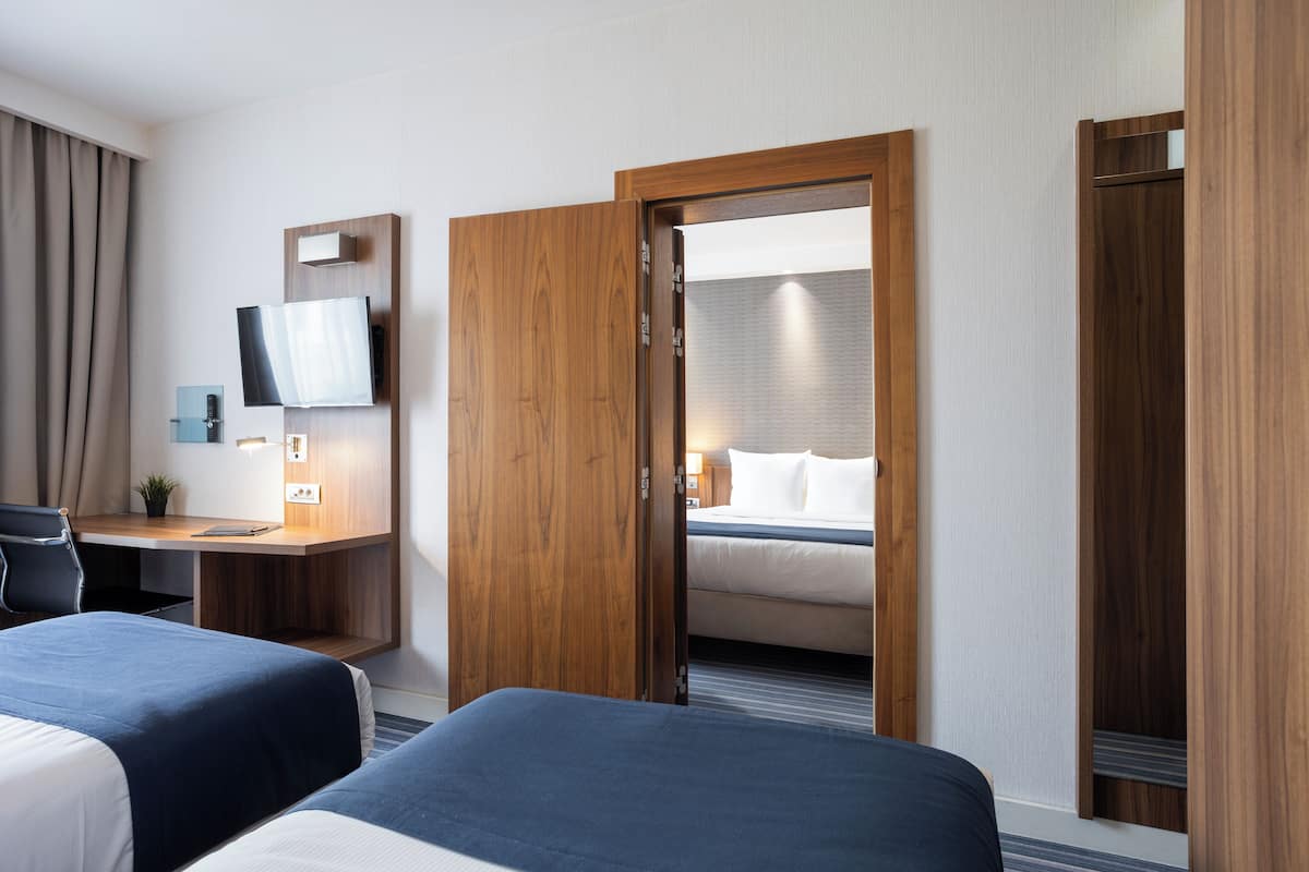 A hotel room with two beds, a desk, a TV, and a mirror.