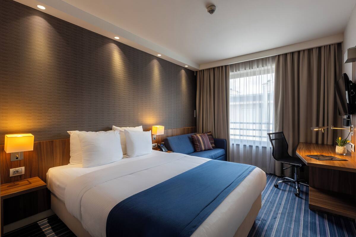 A hotel room with a large bed, a desk, a chair, and a TV.