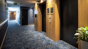 A hotel hallway with wooden doors, a patterned carpet, and a potted plant. - Nobel Palace Hotel (Belgrade)