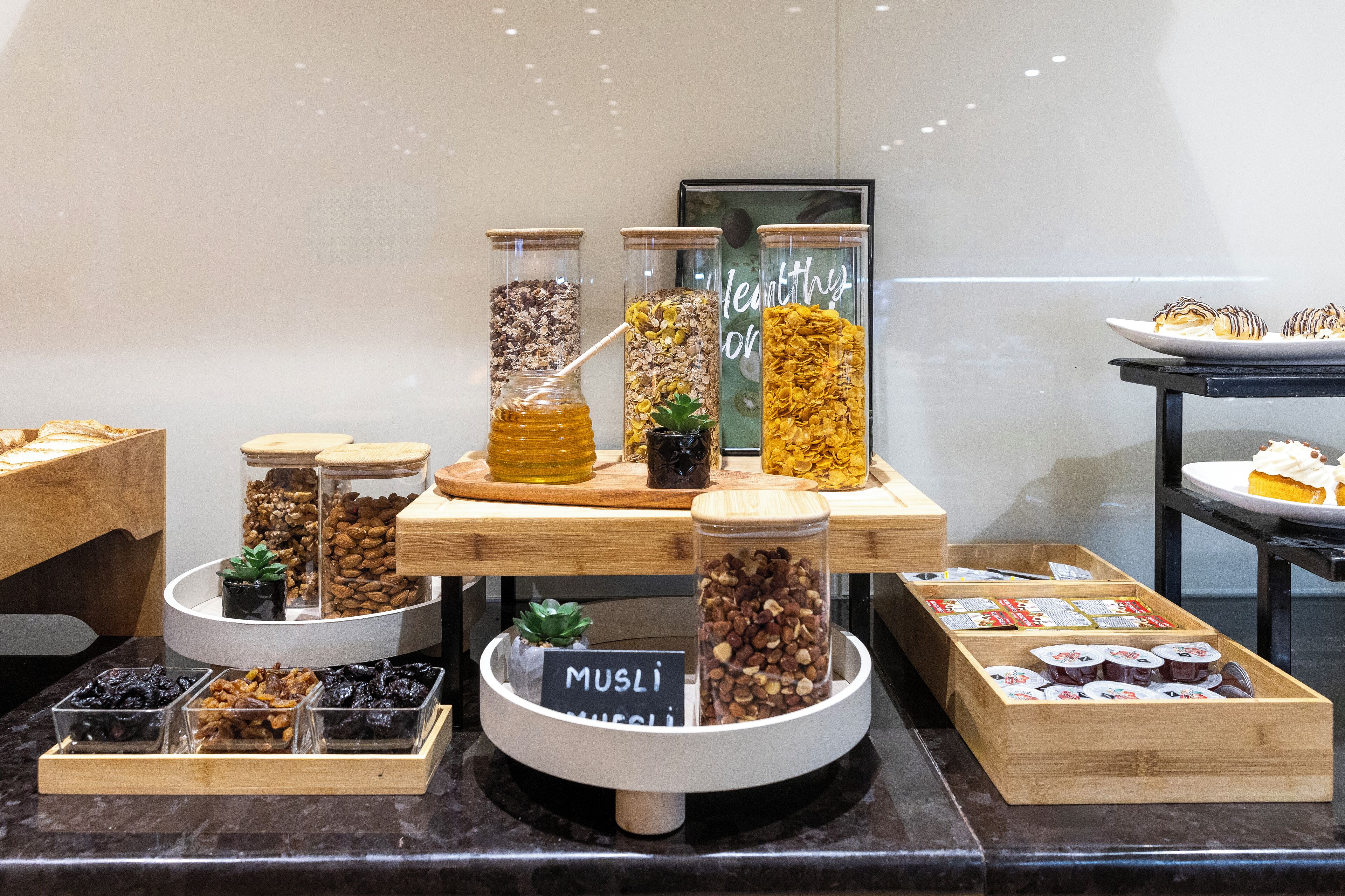 A food display with various jars of nuts and dried fruits, a sign labeled "MUSLI MUSLI", and a plate of pastries.