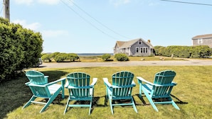 Trois chaises Adirondack turquoise, disposées face à une maison qui offre une vue sur l’océan.